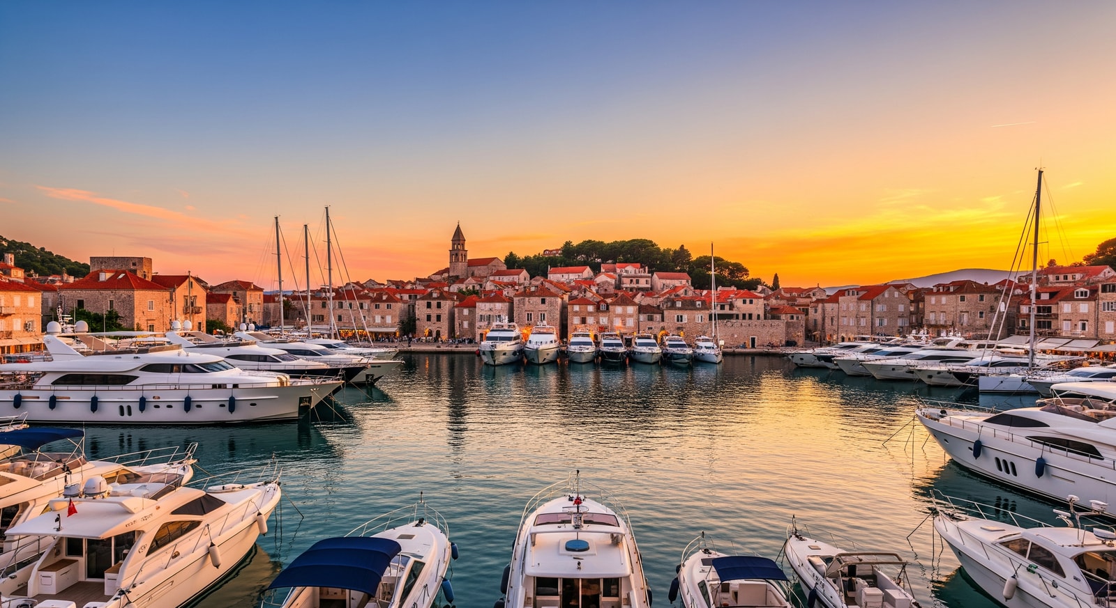 Scenic harbor of Hvar town with luxury yachts and historic Venetian architecture at sunset