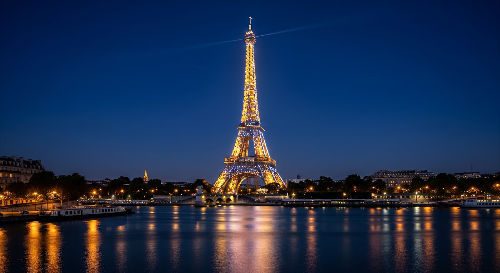 Eiffel Tower illuminated at night with sparkling lights reflecting on the Seine River in Paris