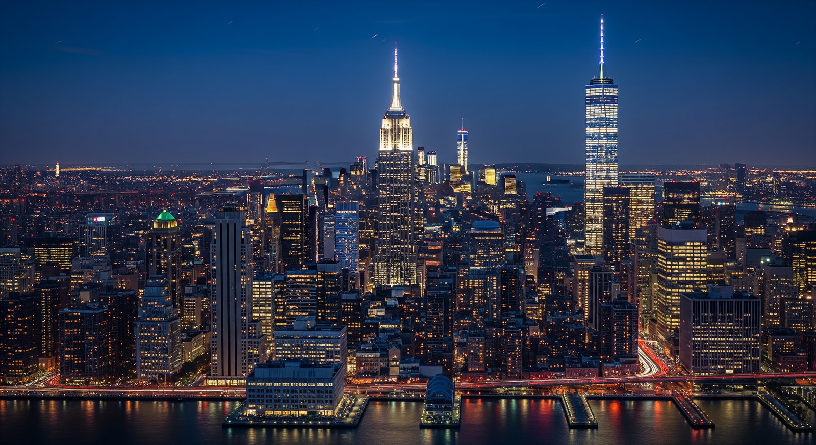 Spectacular night view of Manhattan skyline with Empire State Building and One World Trade Center illuminated against the dark sky
